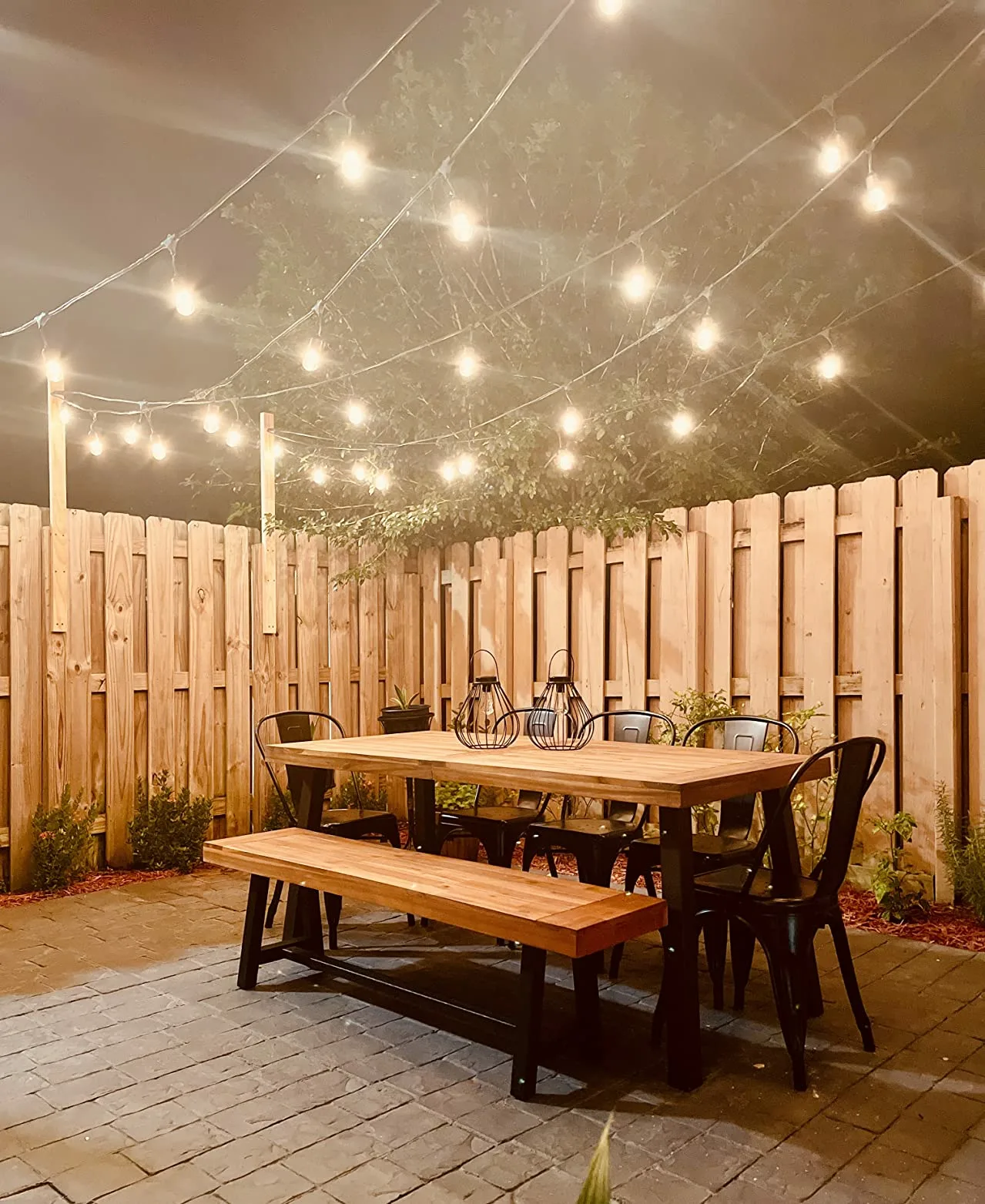 Brown Table Wooden Rectangle Black Chairs Warm Stringlights Wooden Backyard Fence Angle View Custom Made Dining Tables