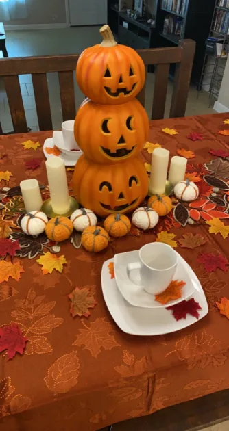 Orange Tablecloth Scattered Maple Leaves Pumpkin Candleholder Centerpiece Closeup Thanksgiving Table Decor