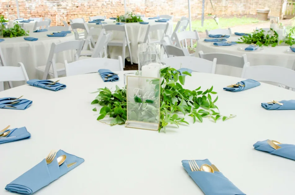 Gold Clear Tablenumber Closeup Dusty Blue Napkins Bright Brick Wall Leaves Centepiece Dinner Table Setting